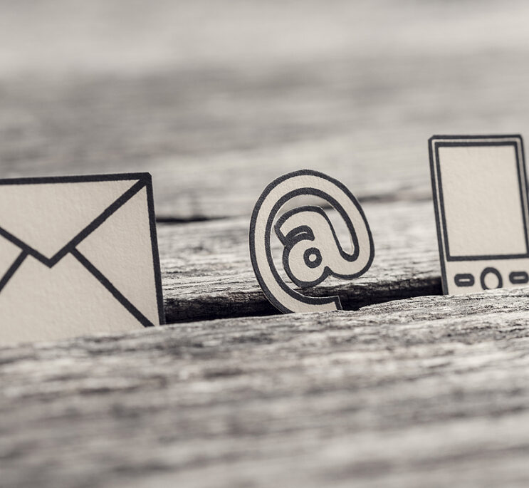 Retro image of business communications concept with icons for email, a web address and telephone on rustic wooden table.